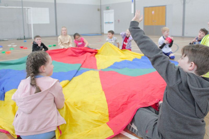 Children using a large sports equipment parachute in 2026 school gym